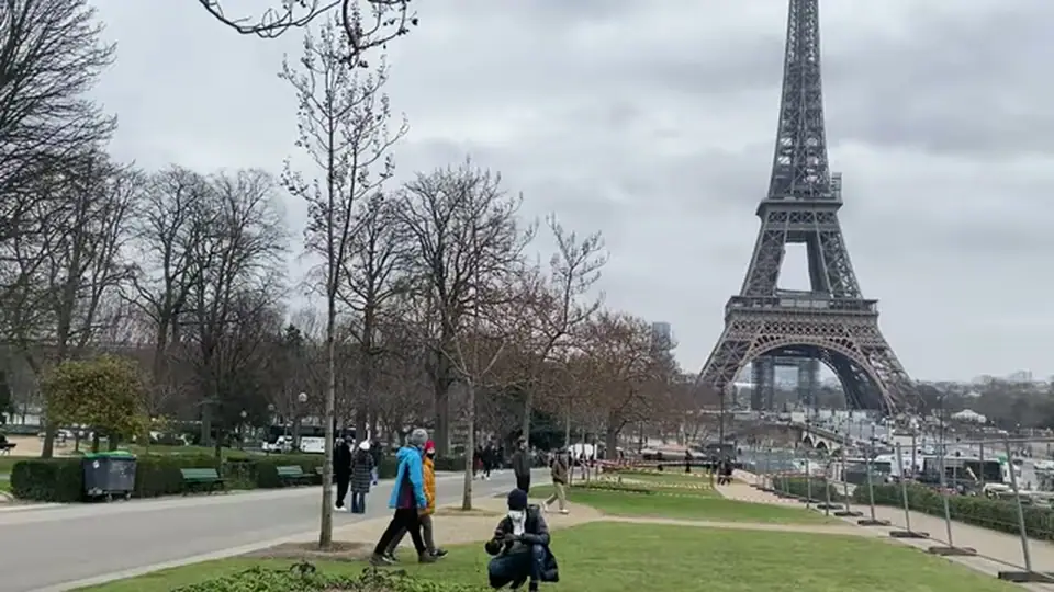 Visitors stroll through a park near the Eiffel Tower by day.