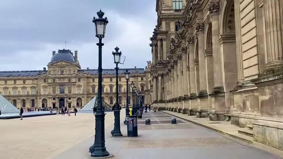 Louvre courtyard with colonnade, lampposts and pyramid under gray sky