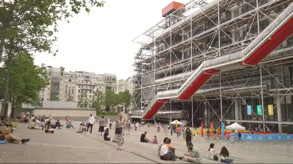 Visitors under trees beside Centre Pompidou’s exposed escalator and pipes