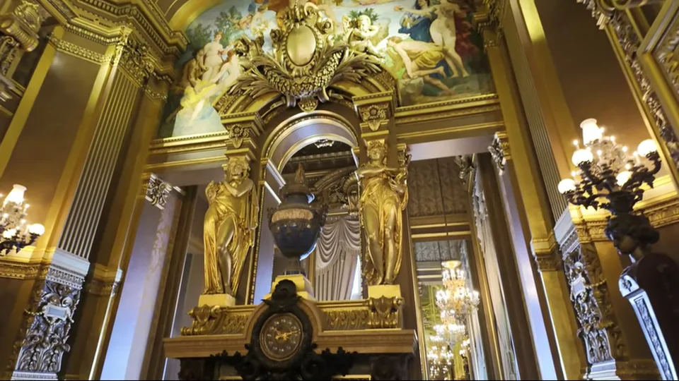 Gilded archway with mural and chandeliers inside Palais Garnier